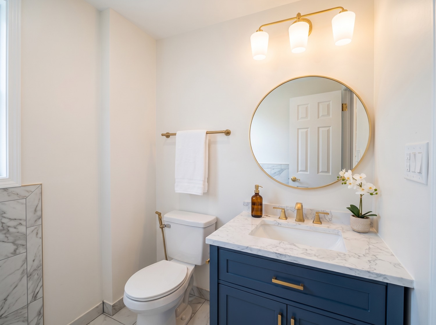 Powder room remodel by Red Carpet with a navy vanity, marble counter, round mirror, and brass fixtures