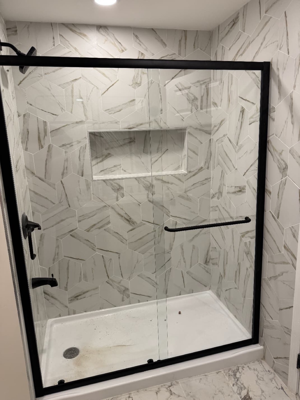 Marble-look tile shower with glass door and built-in niche